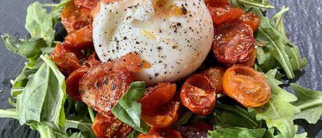 A dish with a poached egg, roasted tomatoes, and arugula on a slate plate.