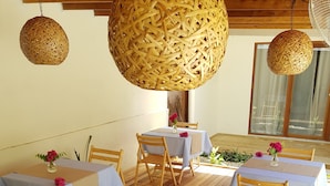 A dining area with tables covered in striped tablecloths, wooden chairs, and hanging woven light fixtures. - Coco Villa (Thoddoo)