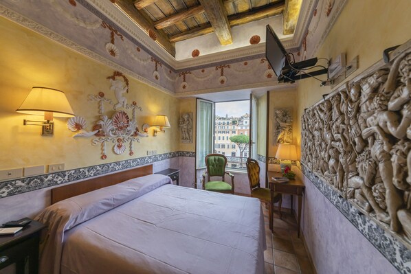 Un cuarto de hotel con una cama grande, dos lámparas de noche, un sillón verde, un escritorio con lámpara y vistas a la ciudad a través de la ventana.