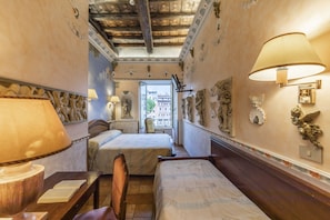 Habitación de hotel con dos camas, un escritorio con lámpara y vista a la ciudad por una ventana.