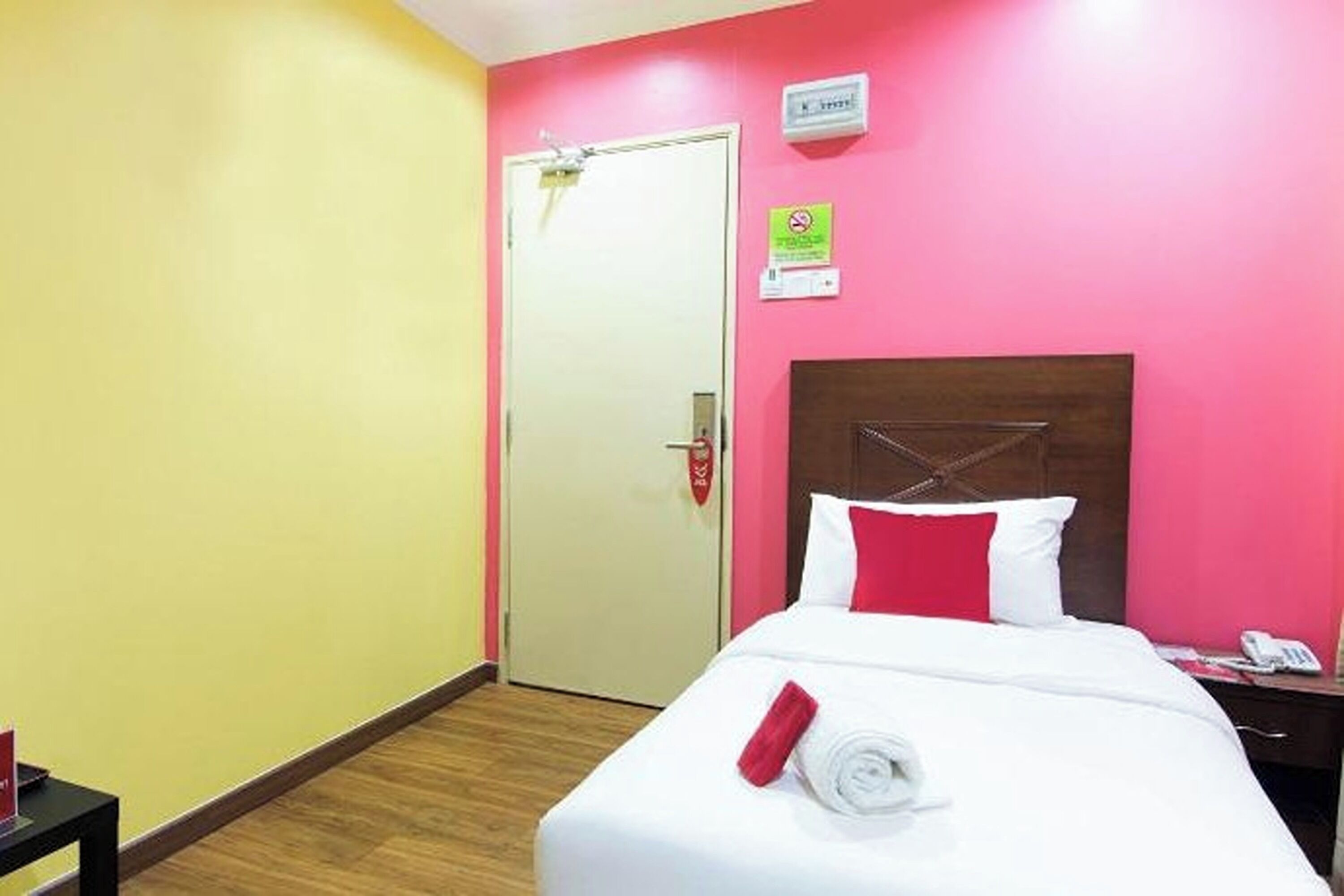 A hotel room with a bed, a bedside table, a nightstand, a door, and a wall sign.