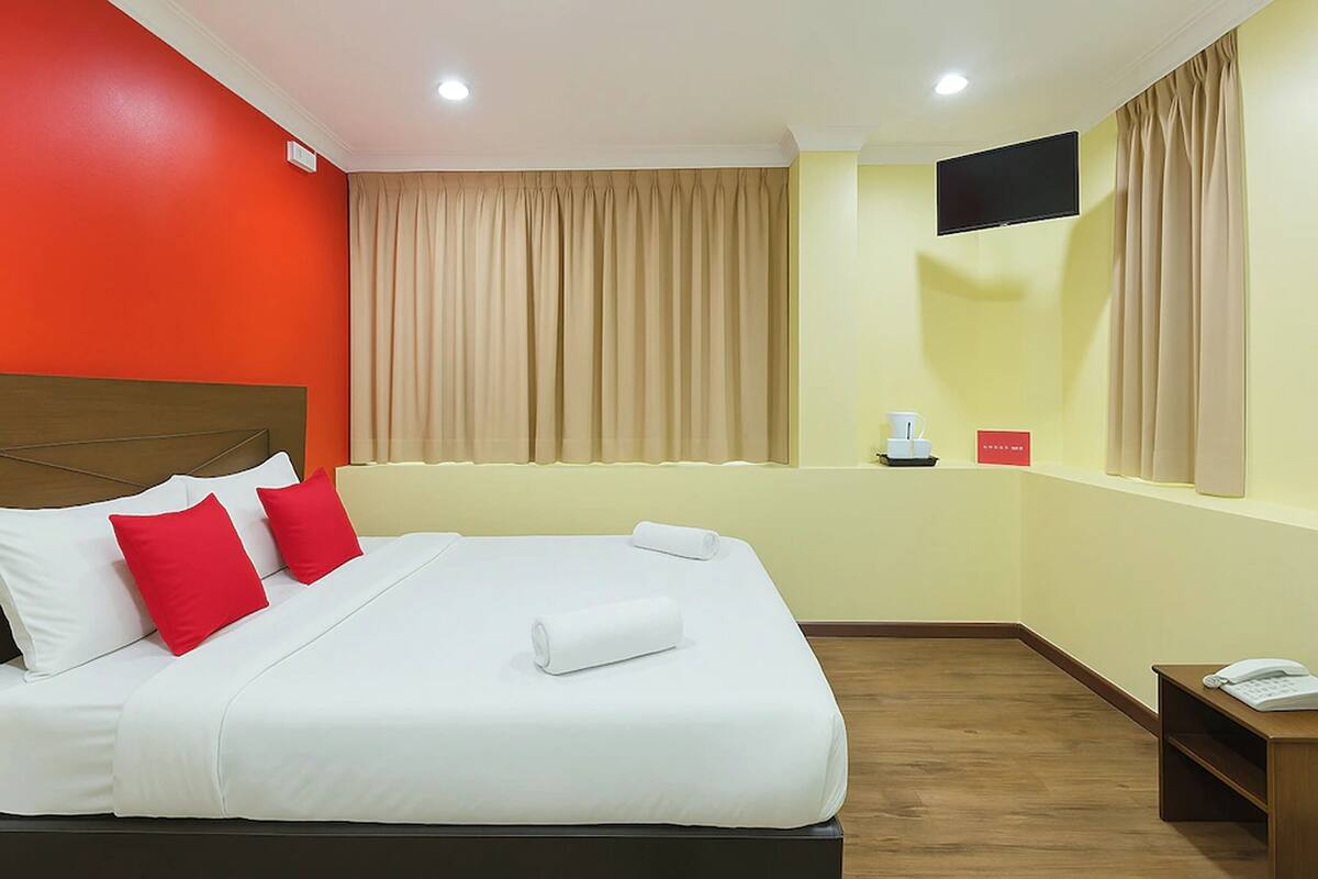 Ein Hotelzimmer mit einem Bett, einem Fernseher, einem Telefon und einem Fenster mit Vorhängen.
