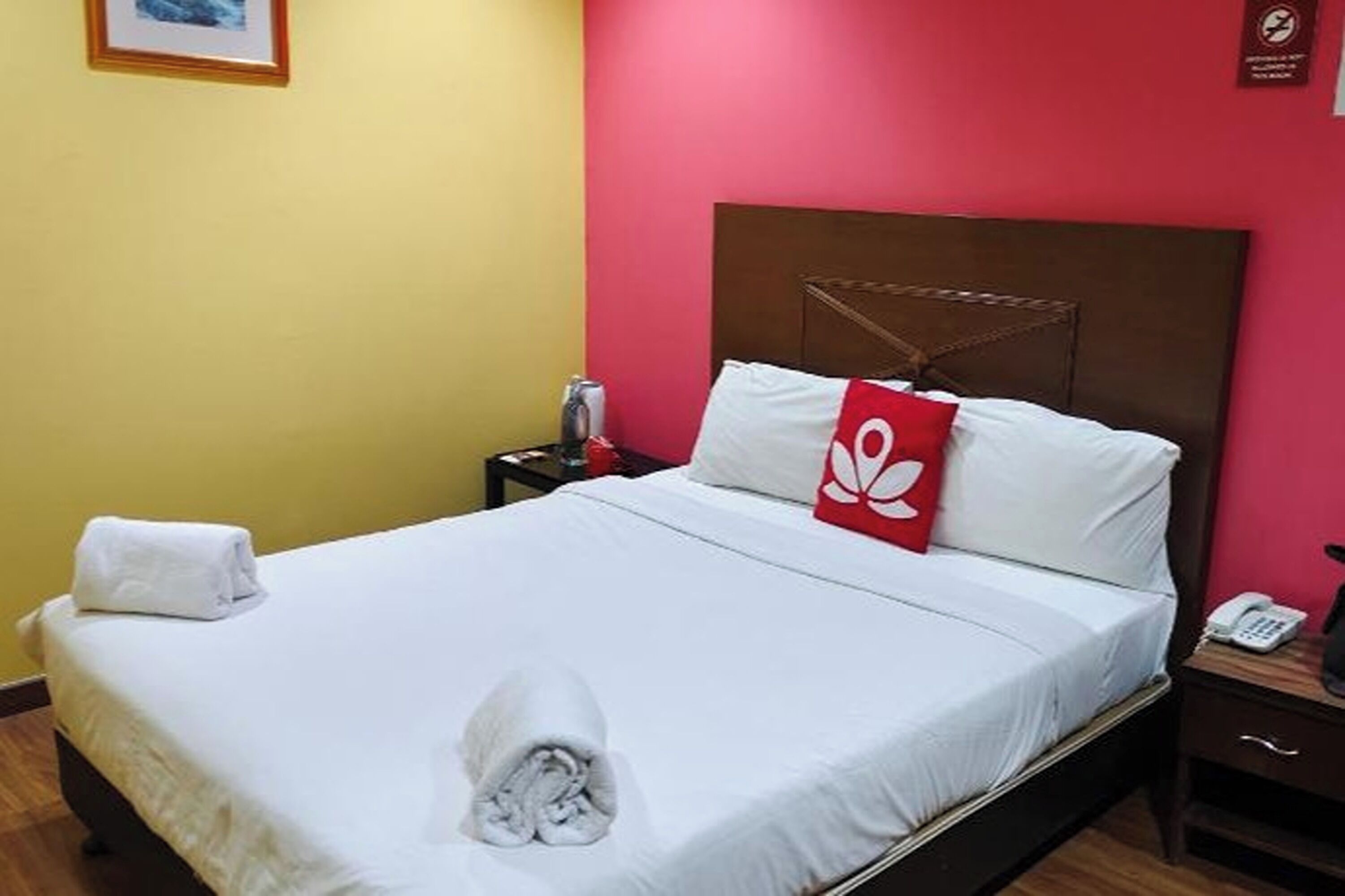 A hotel room with a bed, a nightstand, a red pillow, and a wall-mounted phone.