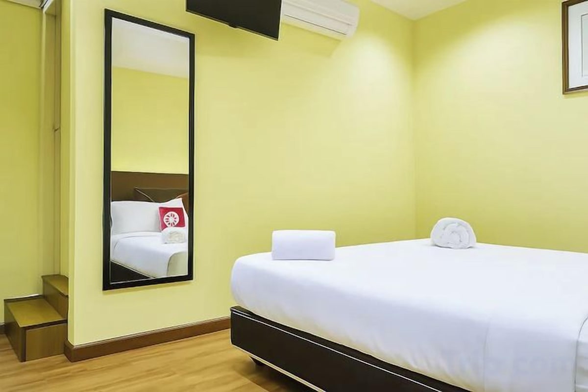 A hotel room with a bed, a mirror, and a small bedside table.