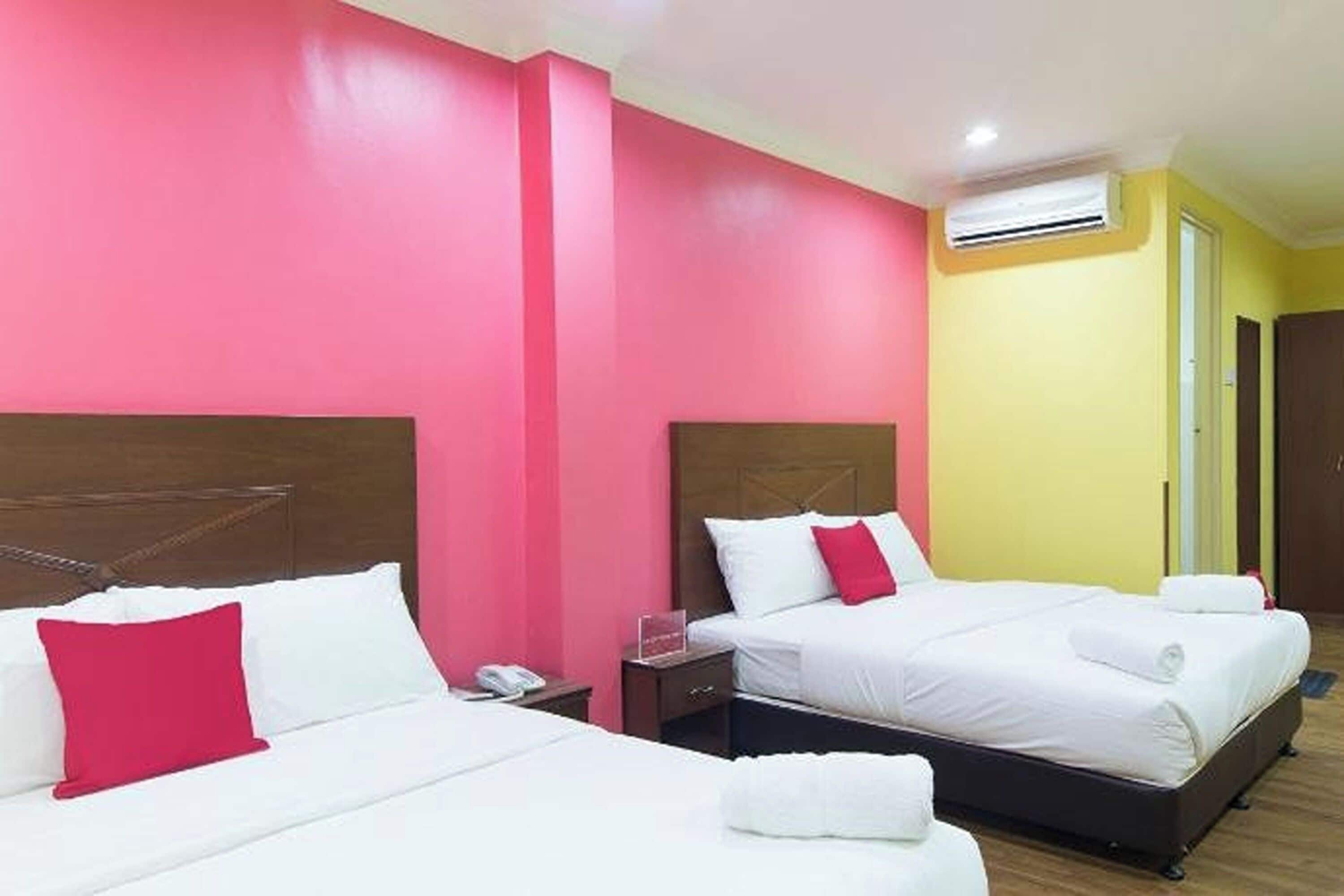 A hotel room with two beds, a wooden headboard, a nightstand, and an air conditioning unit.