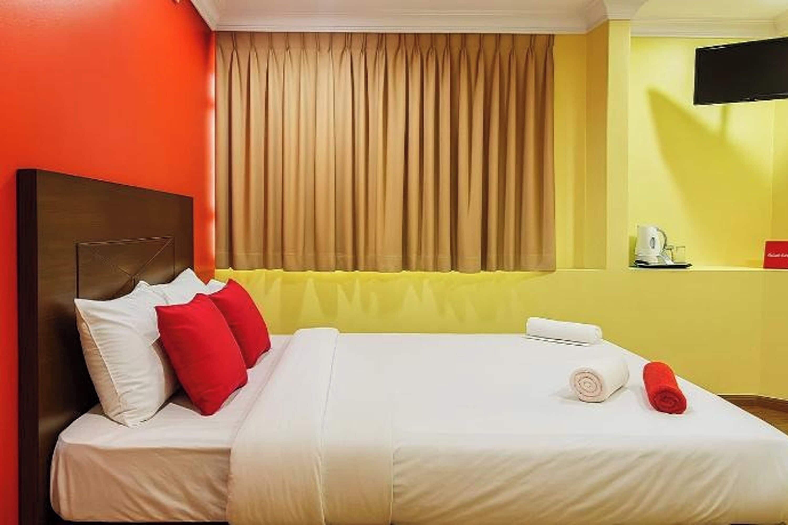 A hotel room with a bed, a headboard, a television, and a window with curtains.
