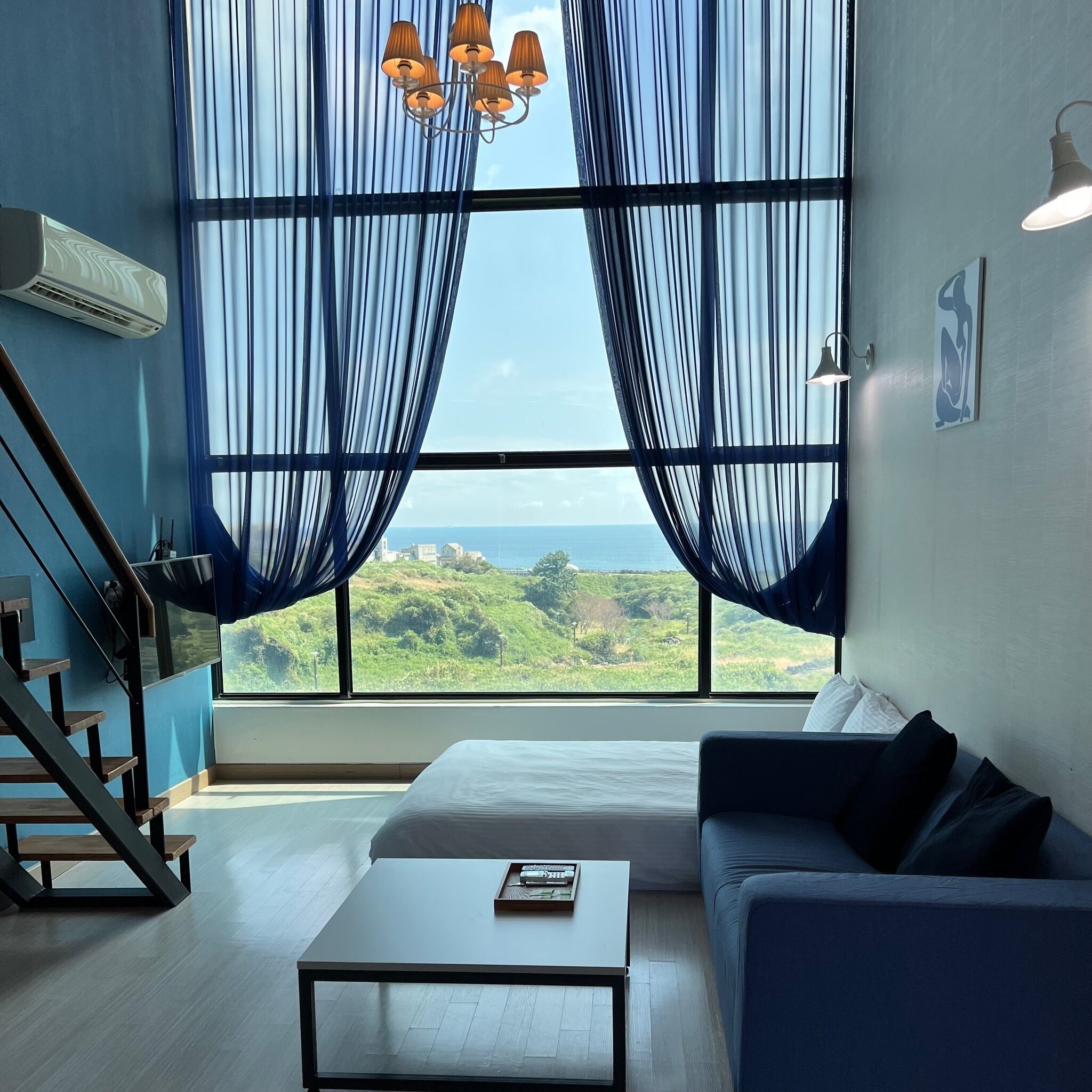A modern living room with a large window, a sofa, a coffee table, and a staircase.