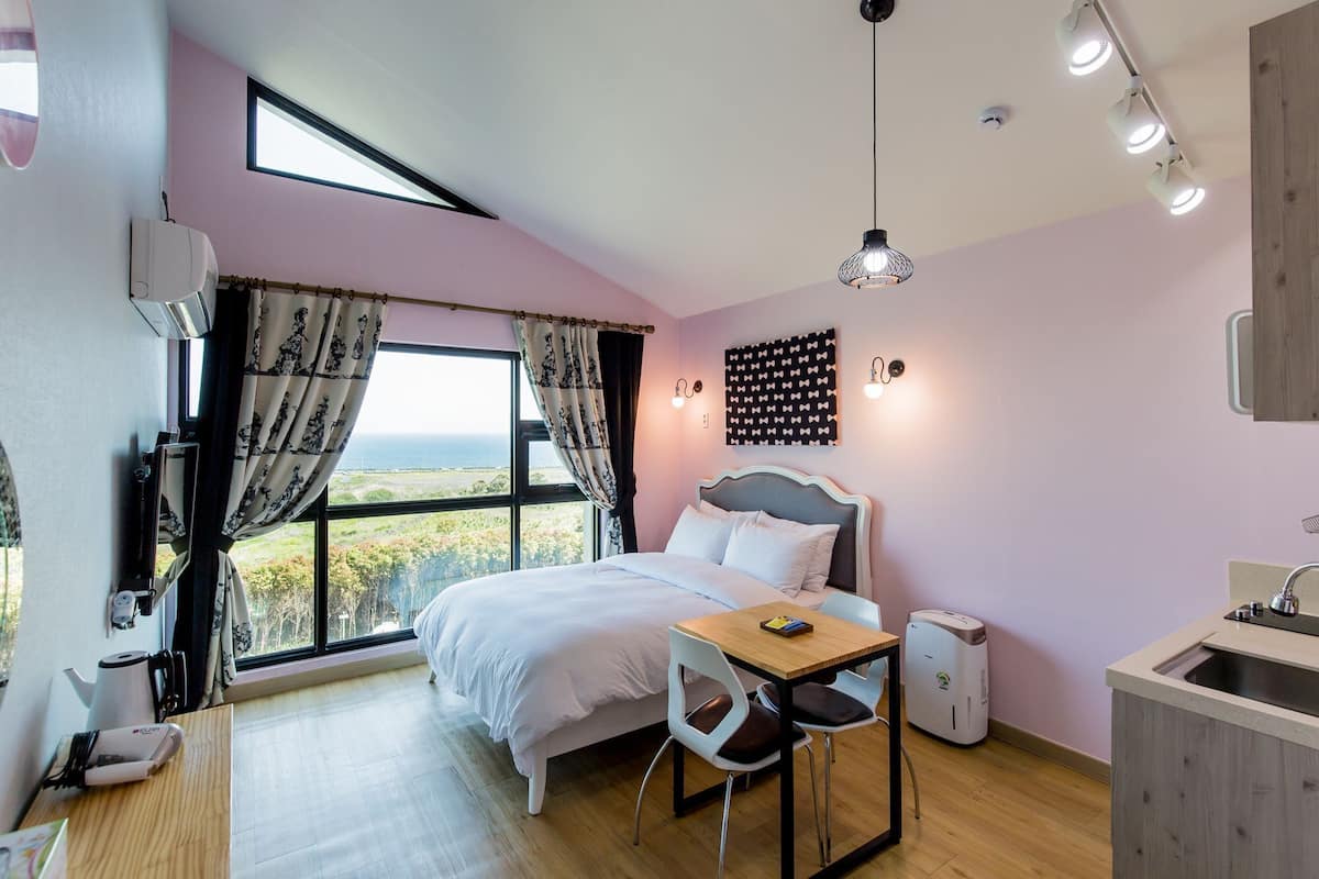 Un dormitorio con cama, una mesa, sillas, una ventana con cortinas, una lámpara de pared y un candelabro de techo.