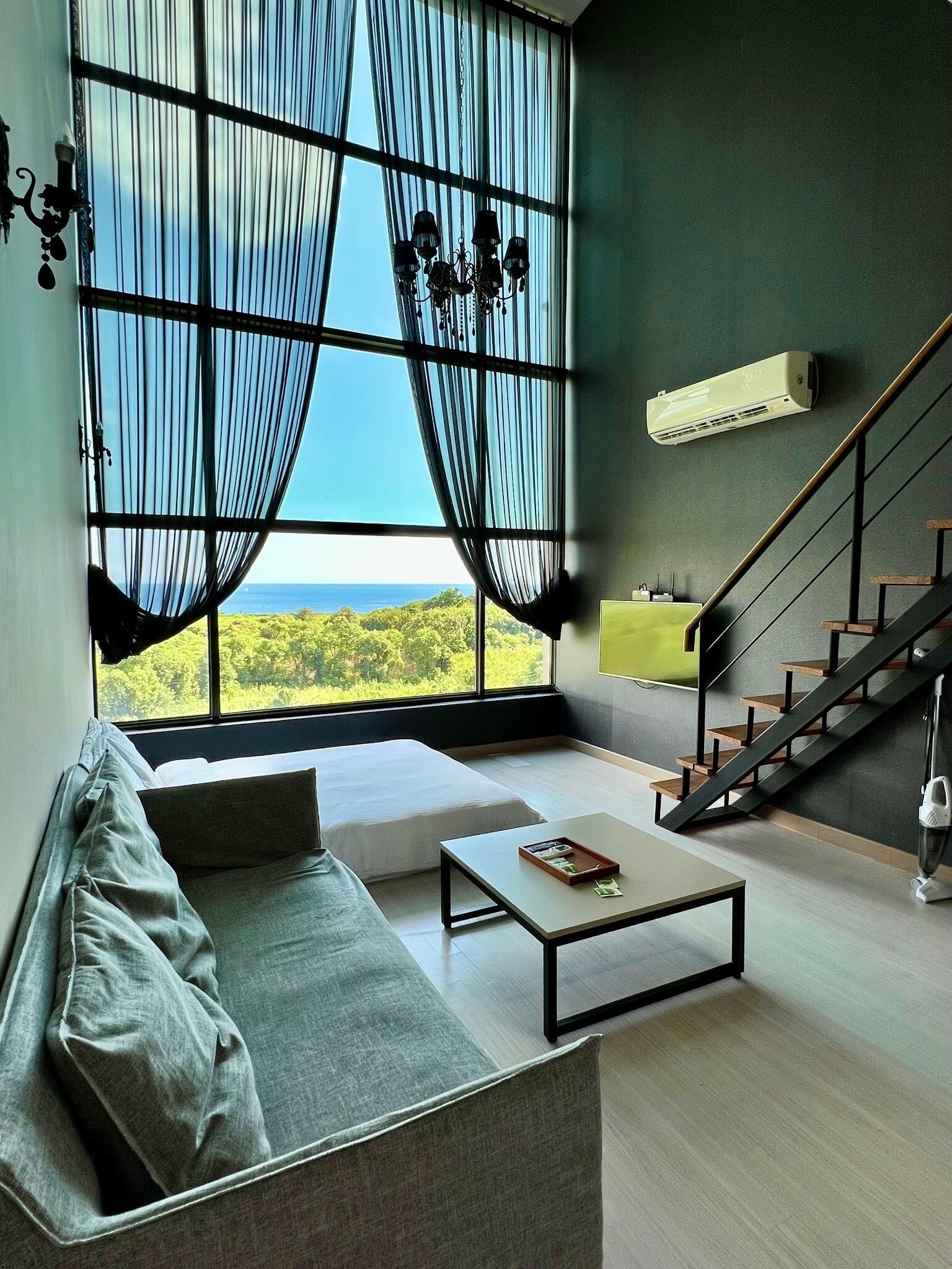 A modern living room with a large window, a staircase, and a sofa.