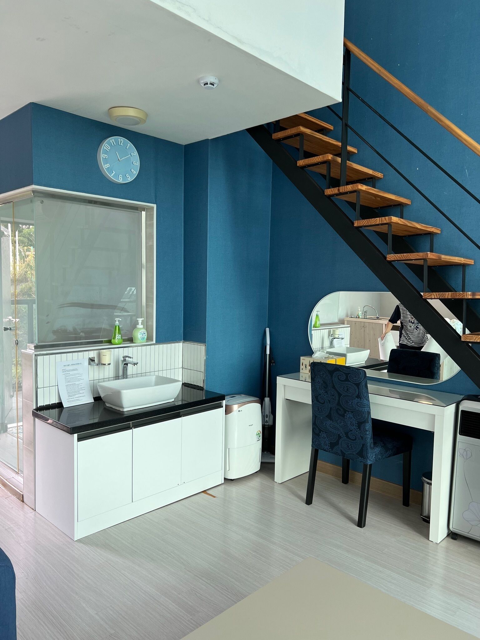 A modern kitchen with a large window, a built-in sink, and a wooden staircase.