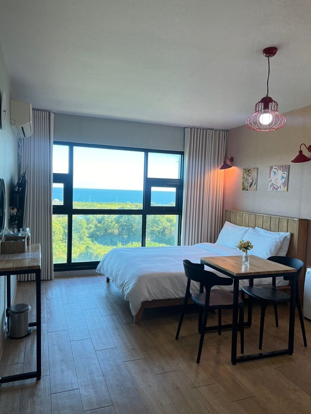 A hotel room with a large window, a bed, a desk, and a chair.