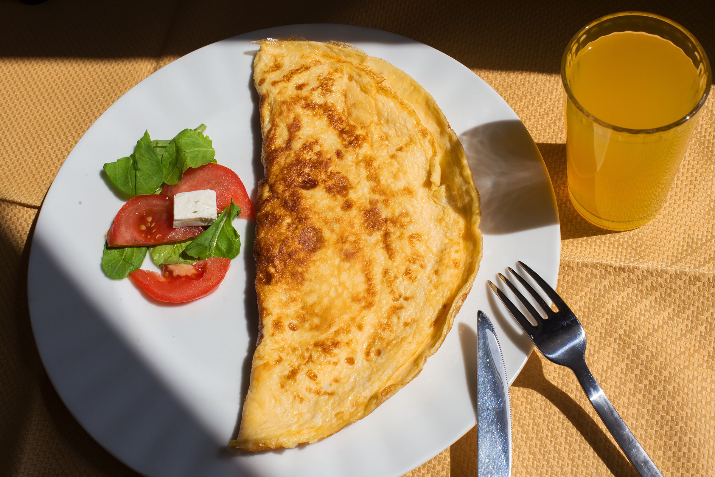 Un plato con una tortilla enrollada, una rodaja de tomate, una hoja de lechuga, un trozo de queso y un vaso de líquido amarillo.