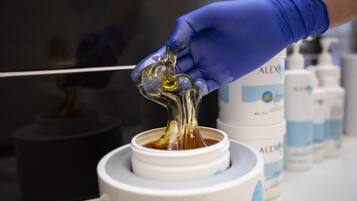 A hand in a blue glove pouring a clear liquid into a white container.