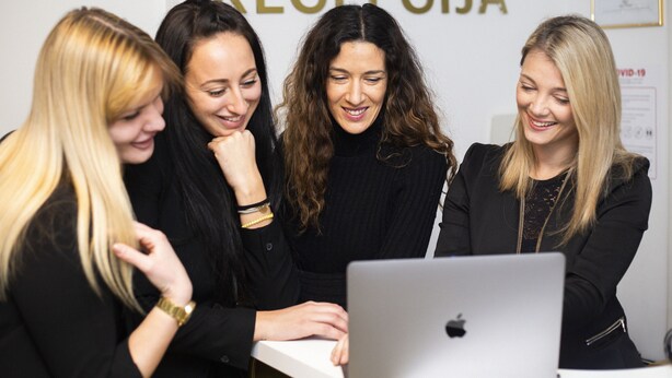 Four individuals gathered around a laptop in a room with a white wall and a sign that reads "RECEPCJA". - B Gold Luxury Rooms (Split)