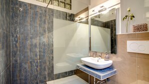 Un baño moderno con cabina de ducha de vidrio, un lavamanos blanco y un espejo grande.