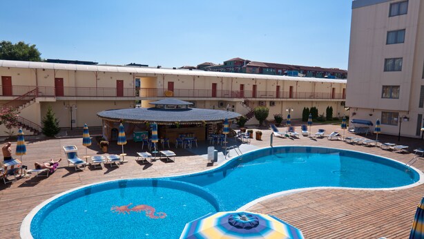 A swimming pool with lounge chairs and umbrellas, a covered area with tables and chairs, and a building with multiple balconies. - Central Plaza Apart Hotel (Sunny Beach)