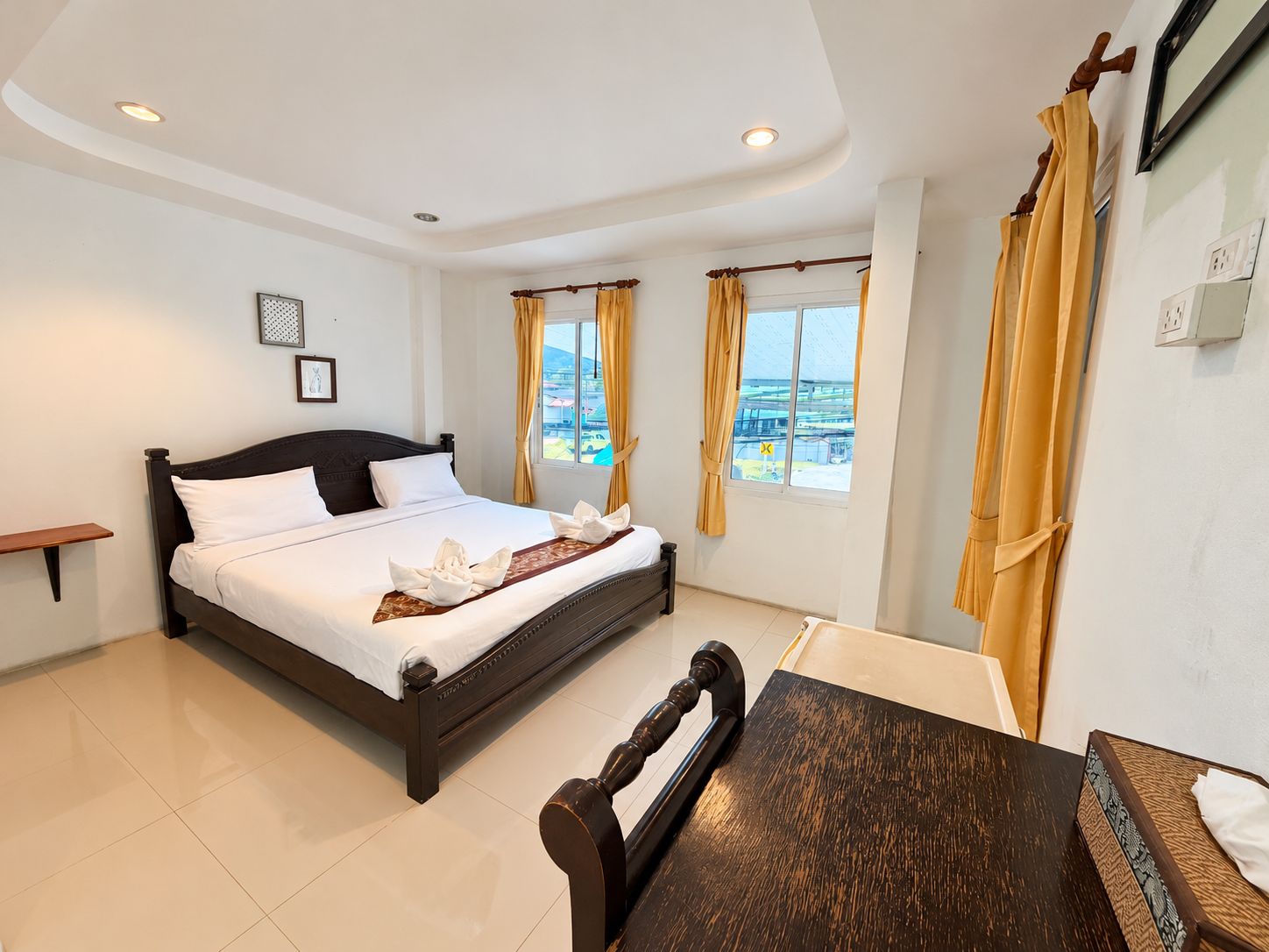 Una habitación de hotel con una cama, una mesa de madera y dos ventanas con cortinas.