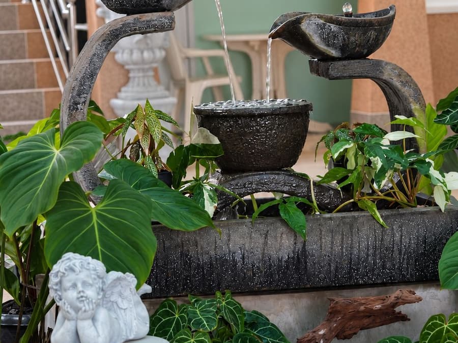 A stone water feature with cascading water, surrounded by potted plants and a decorative angel statue.
