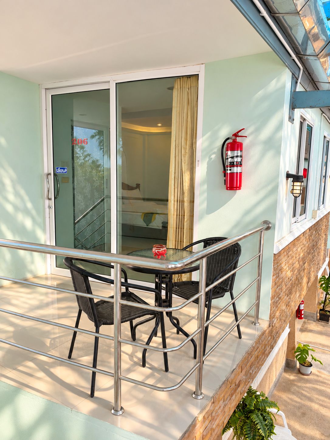 A balcony with a glass door leading to a room, a fire extinguisher mounted on the wall, and a small table with chairs.