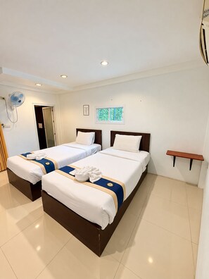 Ein Hotelzimmer mit zwei Betten, einem Deckenventilator, einem kleinen Fenster und einem an der Wand befestigten Regal.