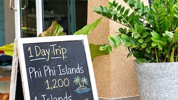 A signboard outside a hotel with a welcome sign, a 1-day trip offer, and a potted plant.