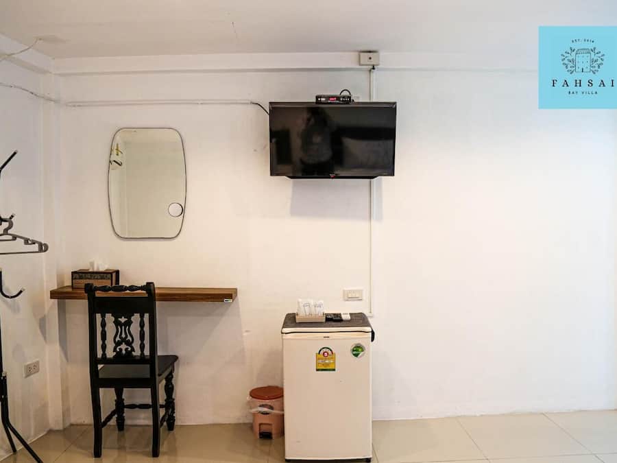 A room with a wooden desk, a chair, a small refrigerator, a coat rack, a mirror, and a television mounted on the wall.