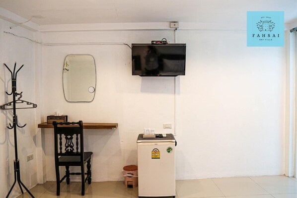 A room with a wooden desk, a chair, a small refrigerator, a coat rack, a mirror, and a television mounted on the wall. - Fahsai Bay Villa (Krabi)