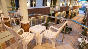 Un balcone con tavolo e sedie, ringhiera in vetro e piante in vaso.