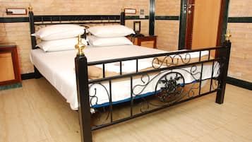 Una cama con estructura metálica y ropa de cama blanca, una mesita de noche de madera y una pared de ladrillo.