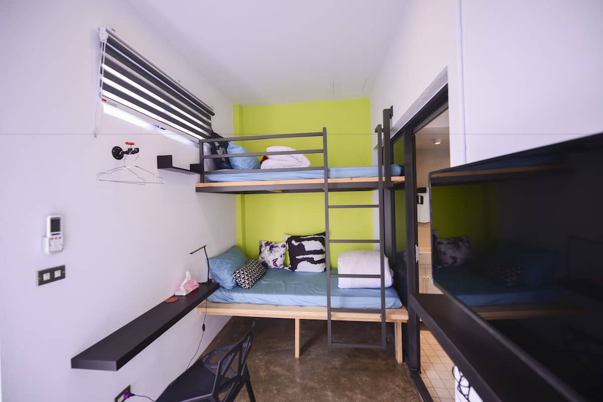 Une chambre avec un lit superposé, un bureau, un porte-manteau et une petite étagère.