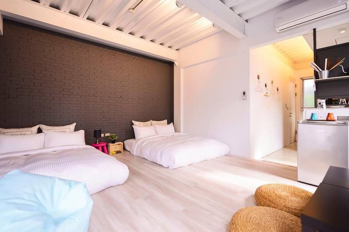 Une chambre moderne avec deux lits, un mur d’accent en briques et un coin cuisine.