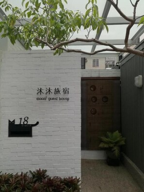 A guest house with a white brick wall, a wooden door, and a small black mailbox with the number 18. - Moon 2 (Tainan)