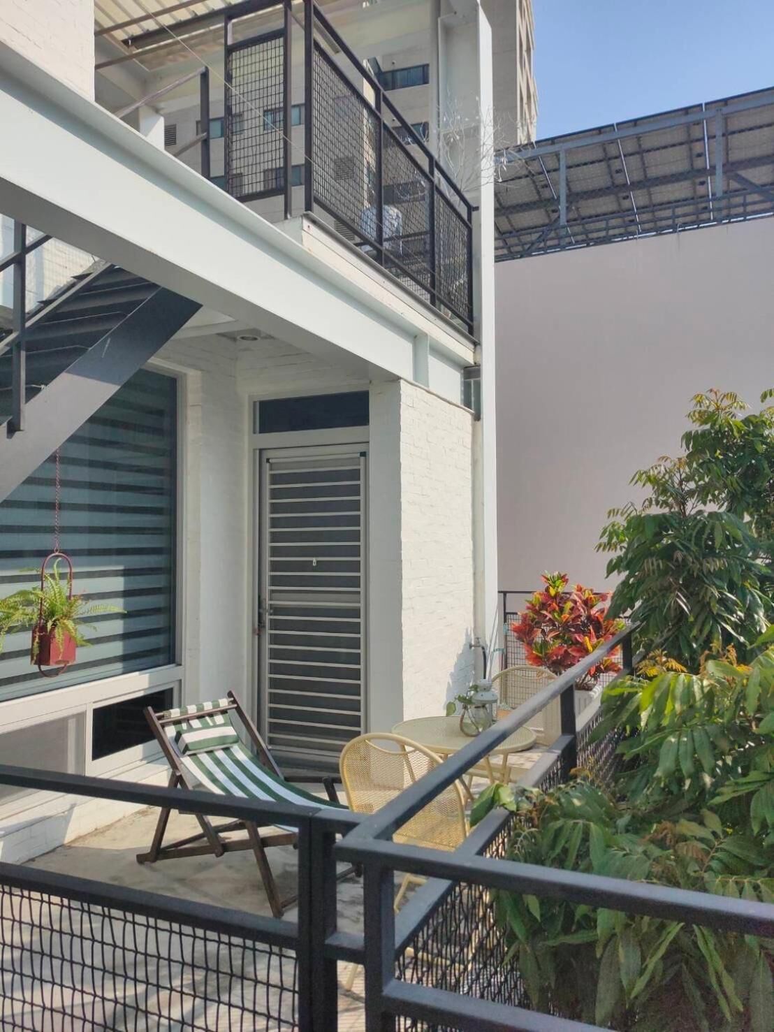 A balcony with a chair, a hanging plant, and a door with a metal gate.