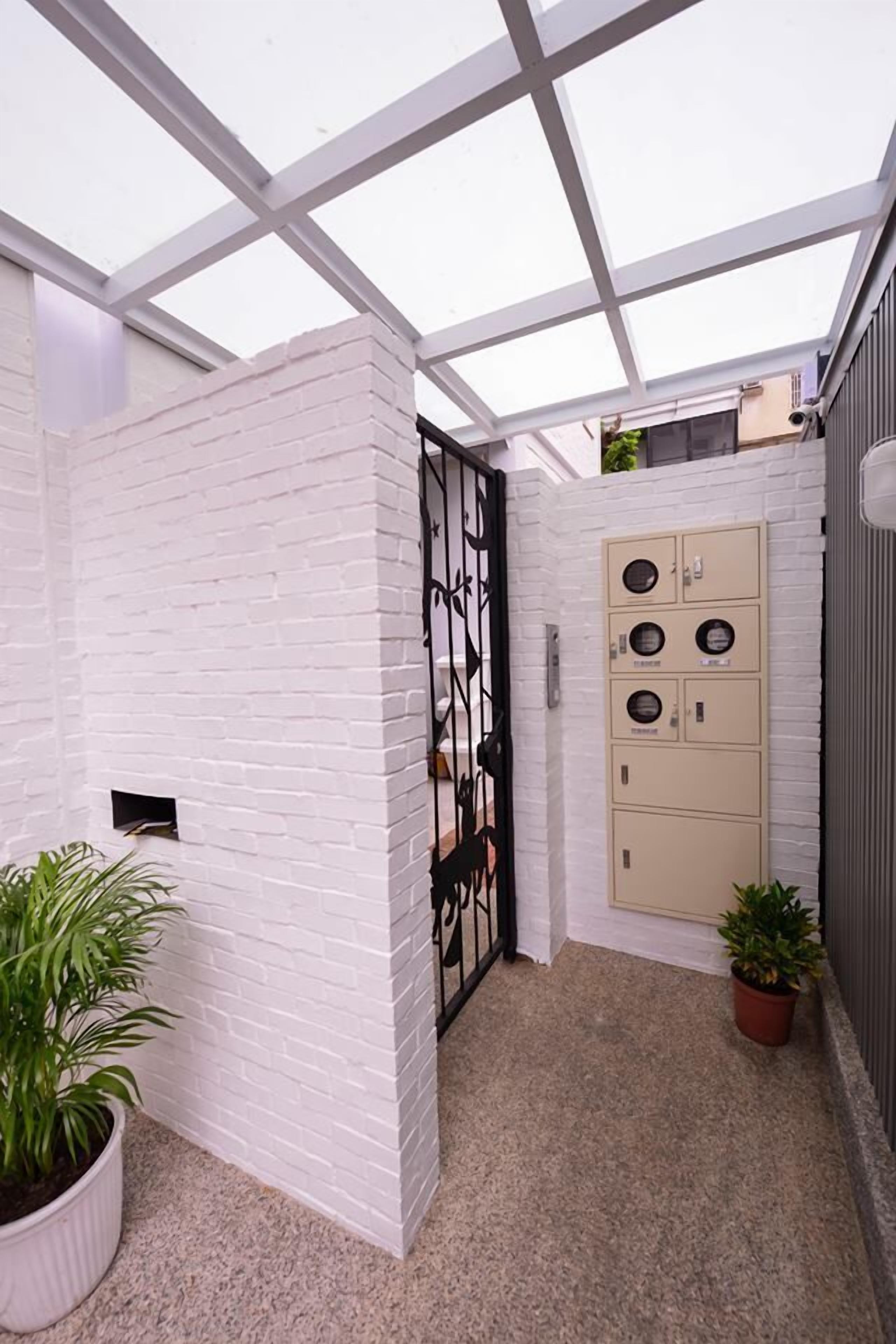 A modern outdoor area with a white brick wall, a metal gate, and a beige utility cabinet.
