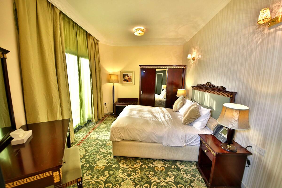 A hotel room with a bed, bedside table, lamp, and a telephone.