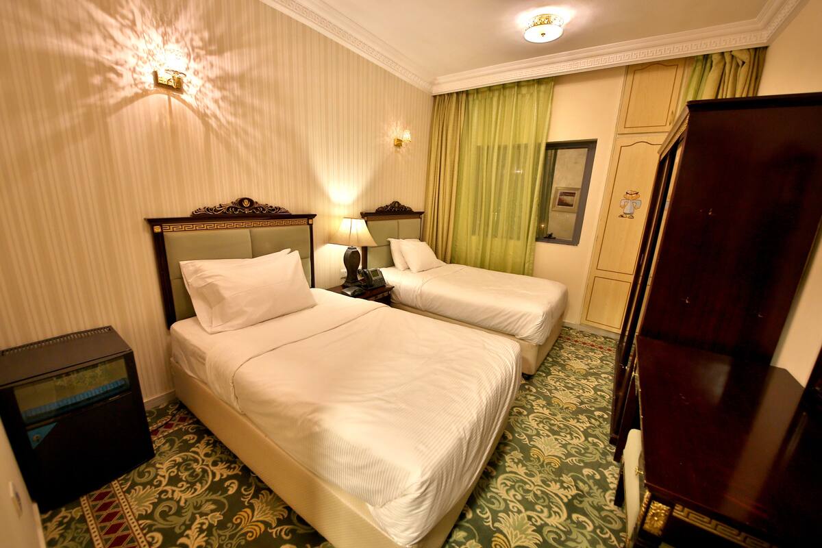 A hotel room with two beds, a nightstand, a lamp, a wardrobe, and a patterned carpet.