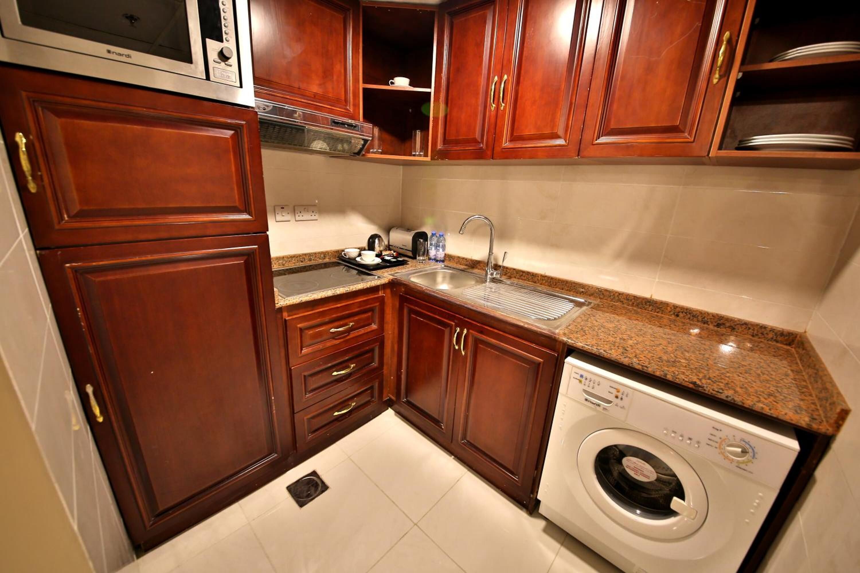 A compact kitchen with wooden cabinets, a built-in microwave, a sink, and a front-loading washing machine.