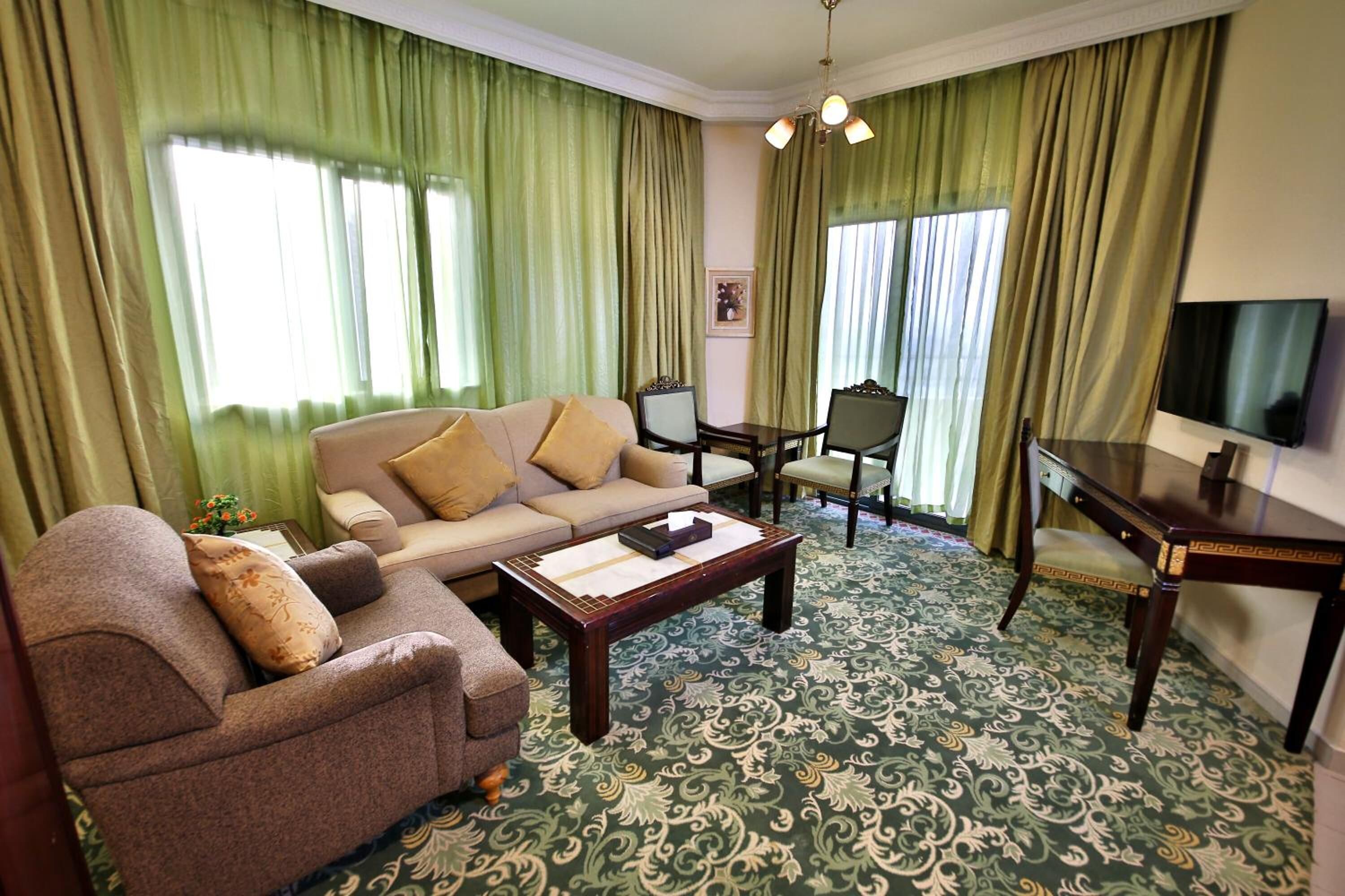 A living room with a sofa, armchairs, a coffee table, a TV, and a patterned carpet.