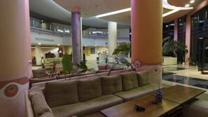 En rummelig lobby med et siddeområde, en restaurant i baggrunden og et moderne arkitektonisk design med store søjler.