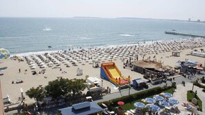 En strand med mange parasoller, en stor oppustelig rutschebane og en mole i baggrunden.
