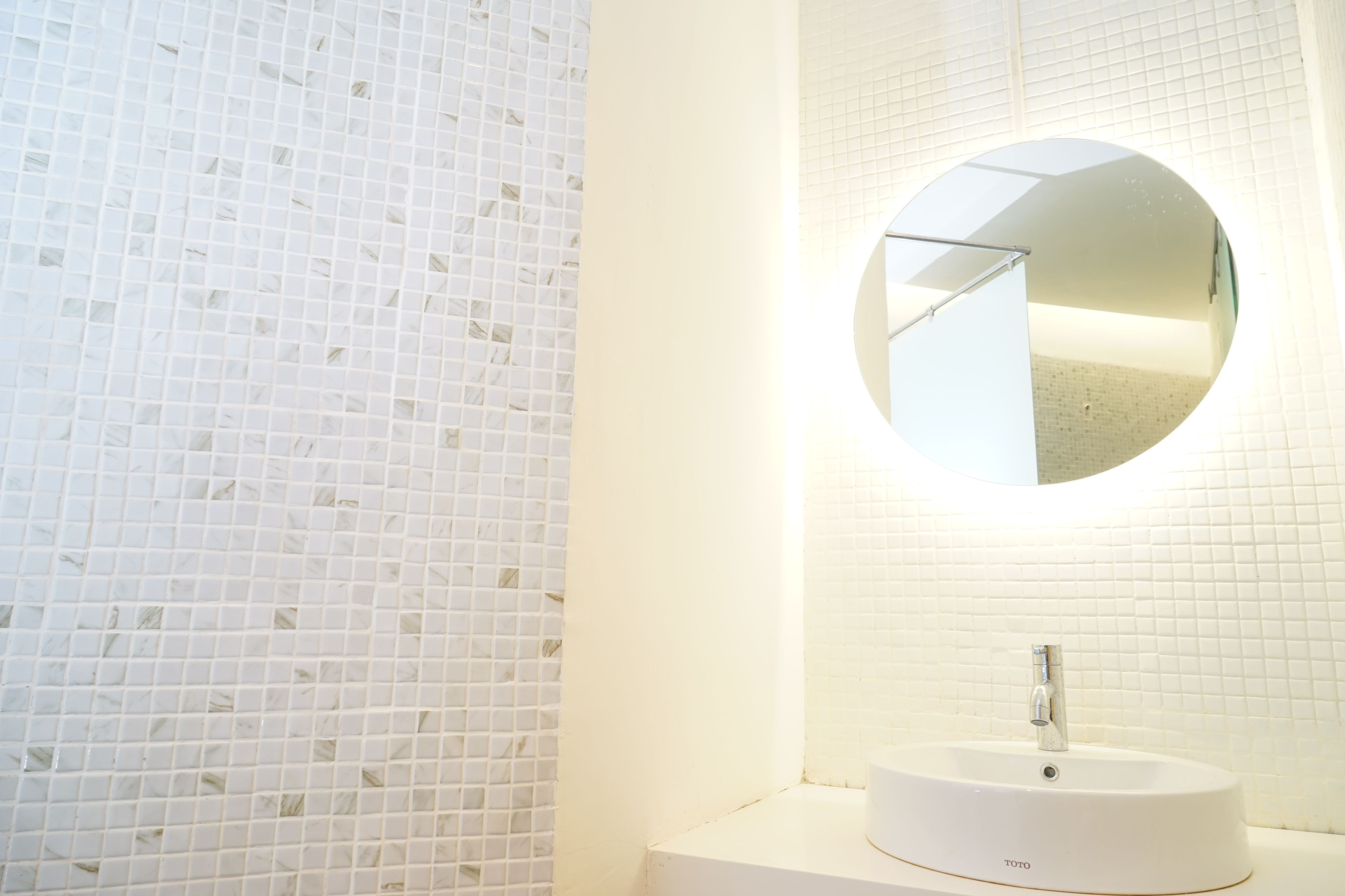 Een badkamer met een witte betegelde wand, een ronde spiegel en een wit wastafelmeubel met een TOTO label.