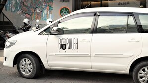 A white car parked in front of a building with a colorful mural and a sign that reads "MORNING GLOBAL". - Borough Capsule Hostel Bali (Legian)