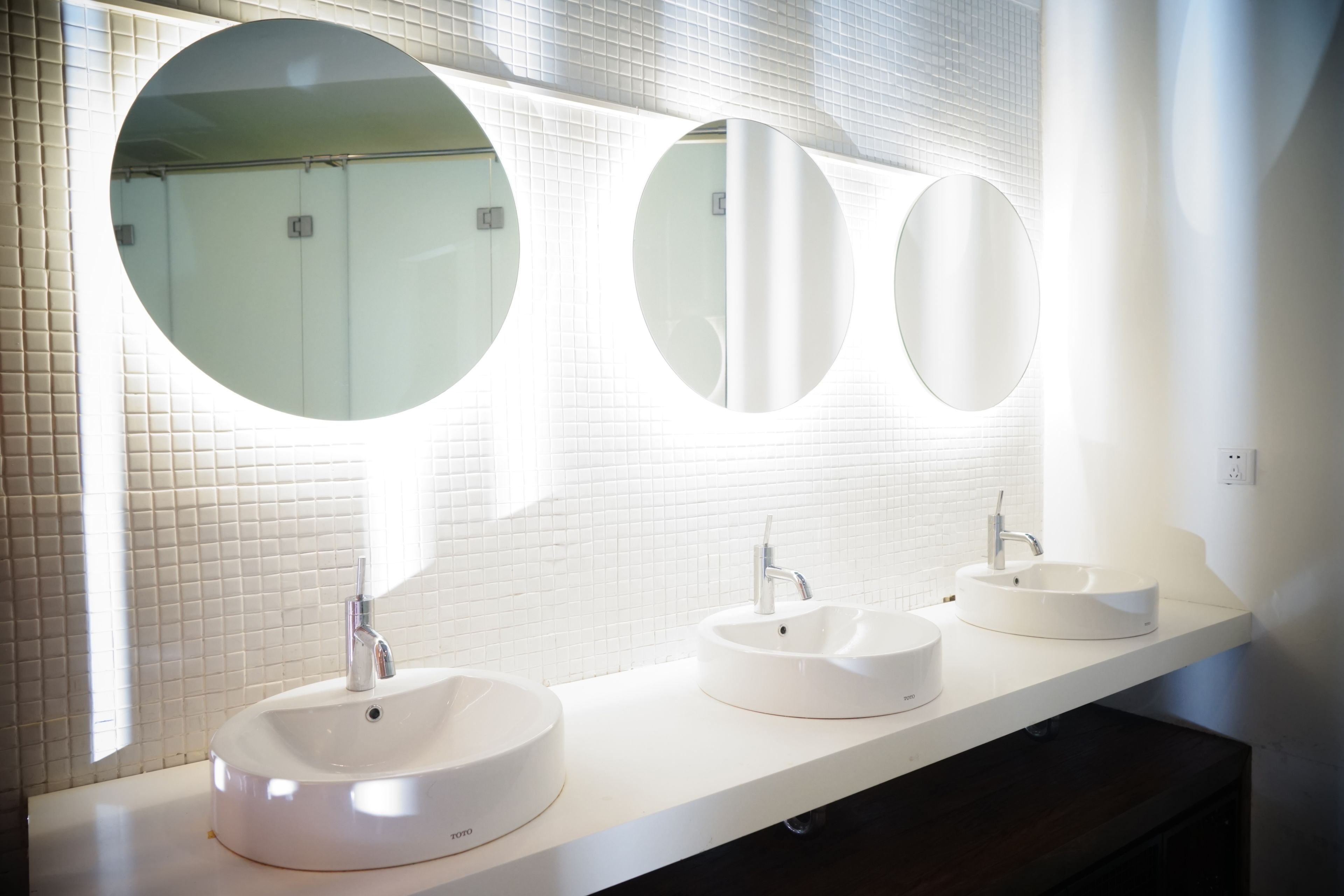 A modern bathroom with three round mirrors and two sinks.