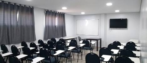 Un salón de conferencias con filas de sillas y mesas, una pizarra y un televisor de pantalla plana en la pared.