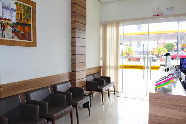 Zona de recepción de hotel con área de espera, un cuadro en la pared y vistas al exterior.
