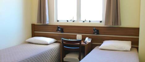 Une chambre d’hôtel avec deux lits, un bureau avec un téléphone et une fenêtre avec des rideaux.