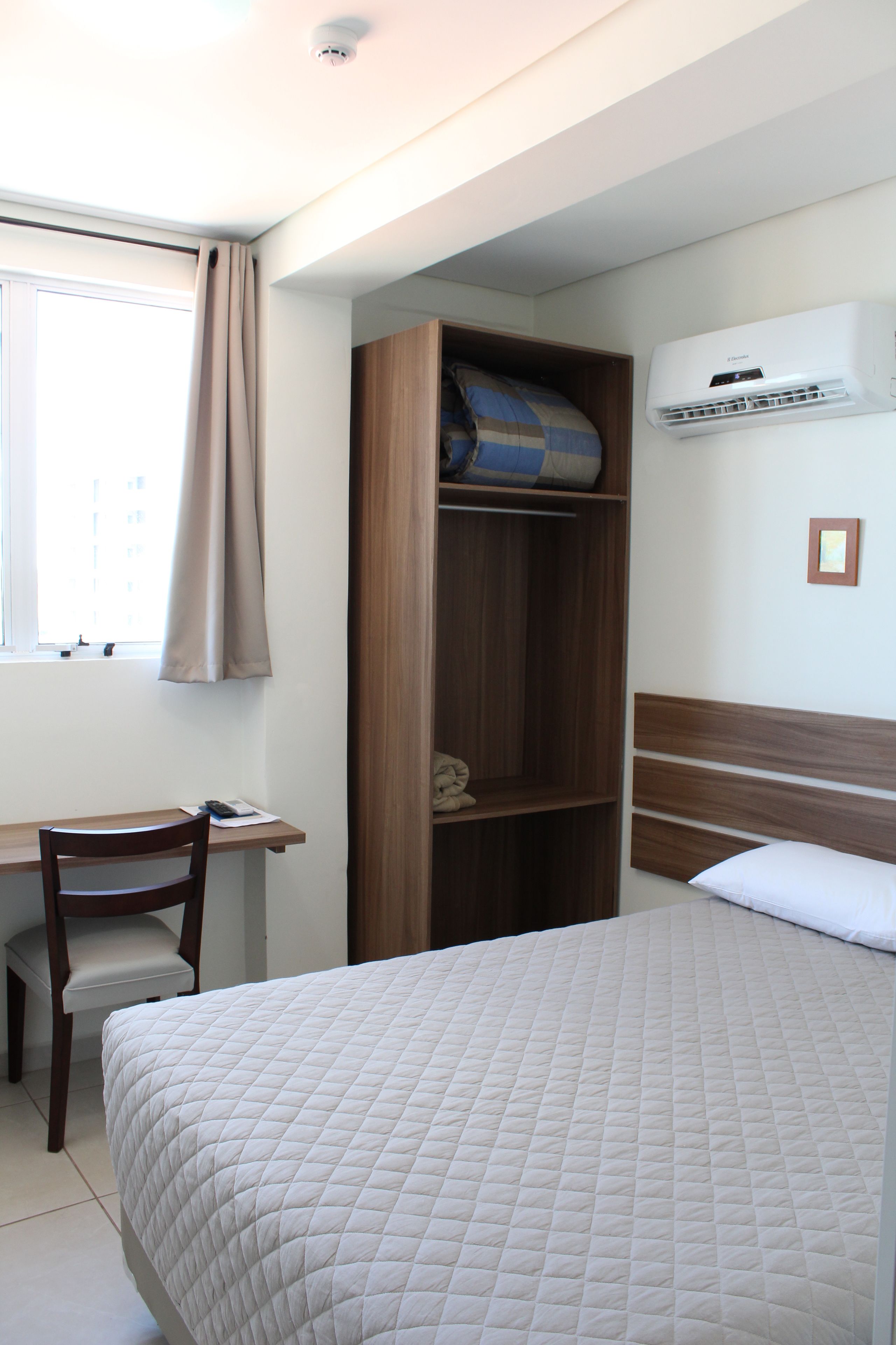 Een slaapkamer met een bed, een bureau, een stoel, een kledingkast en een airconditioning.