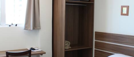 A bedroom with a bed, a desk, a chair, a wardrobe, and an air conditioning unit.