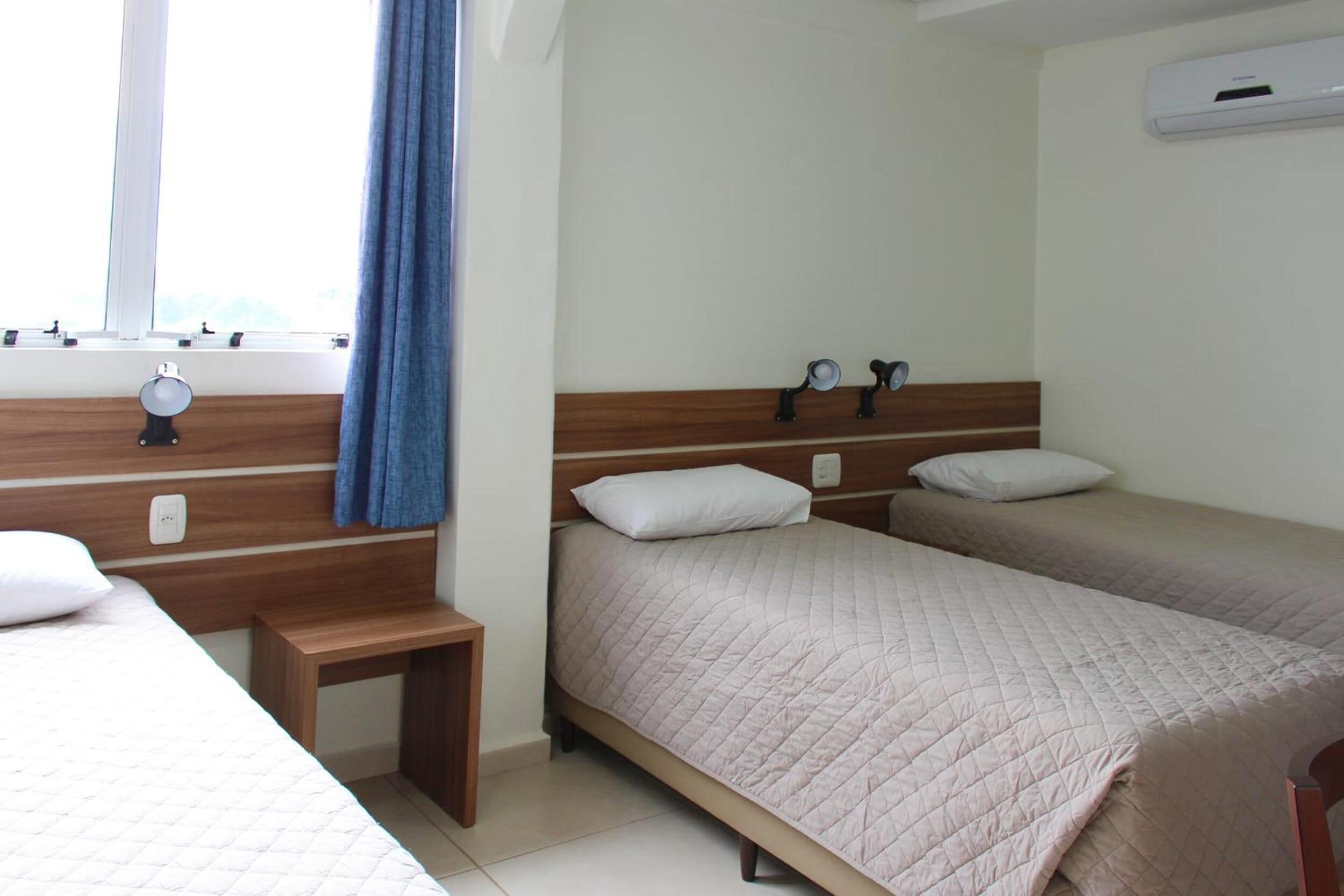 Habitación de hotel con dos camas, una mesita de noche, una ventana con cortinas y un equipo de aire acondicionado.