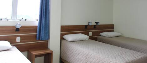 Habitación de hotel con dos camas, una mesita de noche, una ventana con cortinas y un equipo de aire acondicionado.